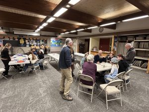 Two groups of people gather at tables, some standing, some sitting, as they play board games in Sandburg Hall