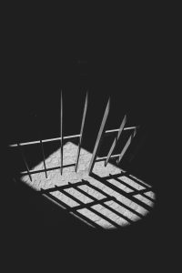 B&W photo of illuminated jail cell bars casting a bright shadow